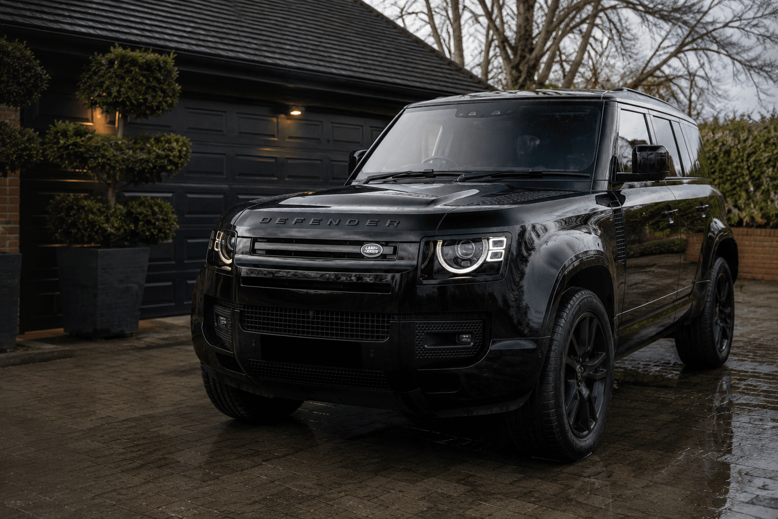 Freshly detailed black Land Rover Defender on a wet driveway